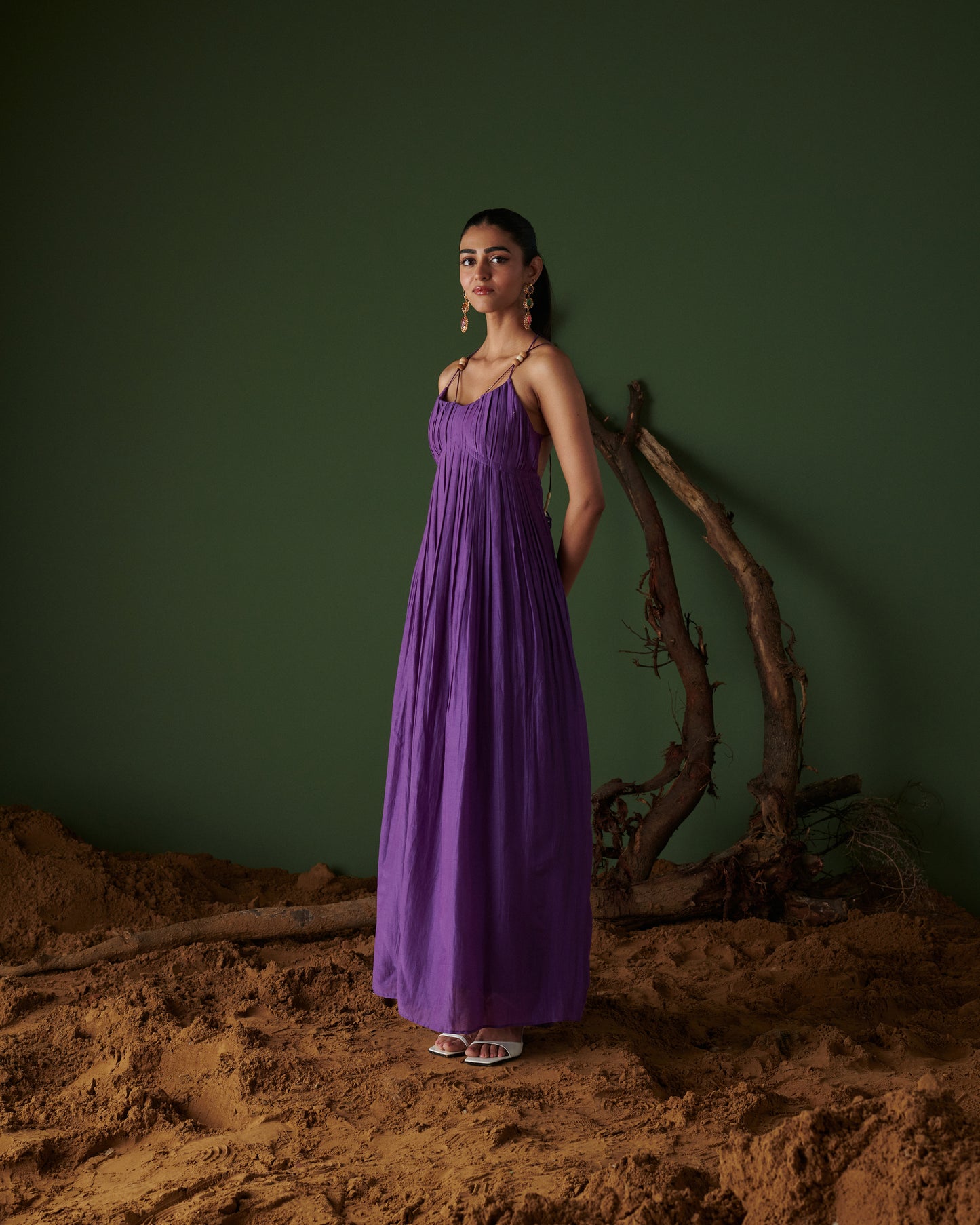 Model wearing Jamun Jalsa Dress in deep purple, flowy pleated maxi with thin straps, styled with statement earrings by Naarangi.