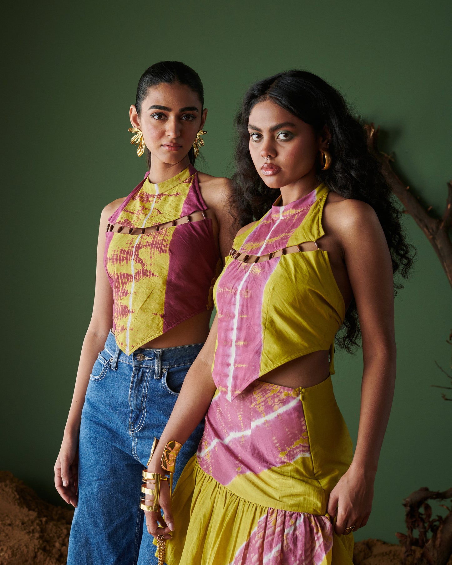 Two models wearing Khatta Jaljeera handcrafted halter-neck tops in mustard yellow and magenta pink tie-dye, one styled with a matching skirt and the other with blue denim, from Naarangi’s Chaska collection.