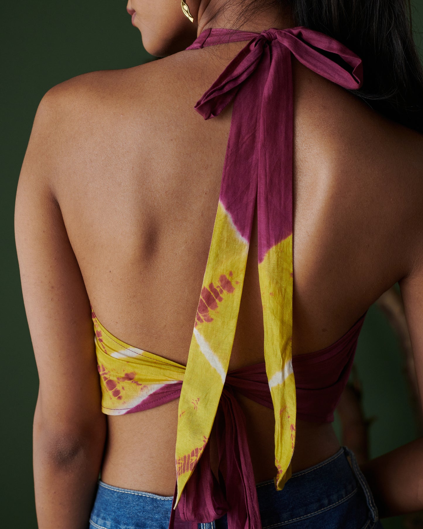Back view of Meetha Jaljeera Top in wine and deep yellow by Naarangi, showcasing halter-neck tie detail, open back design, and hand-dyed traditional patterns, styled with denim for a fusion of ethnic craftsmanship and modern fashion in India.