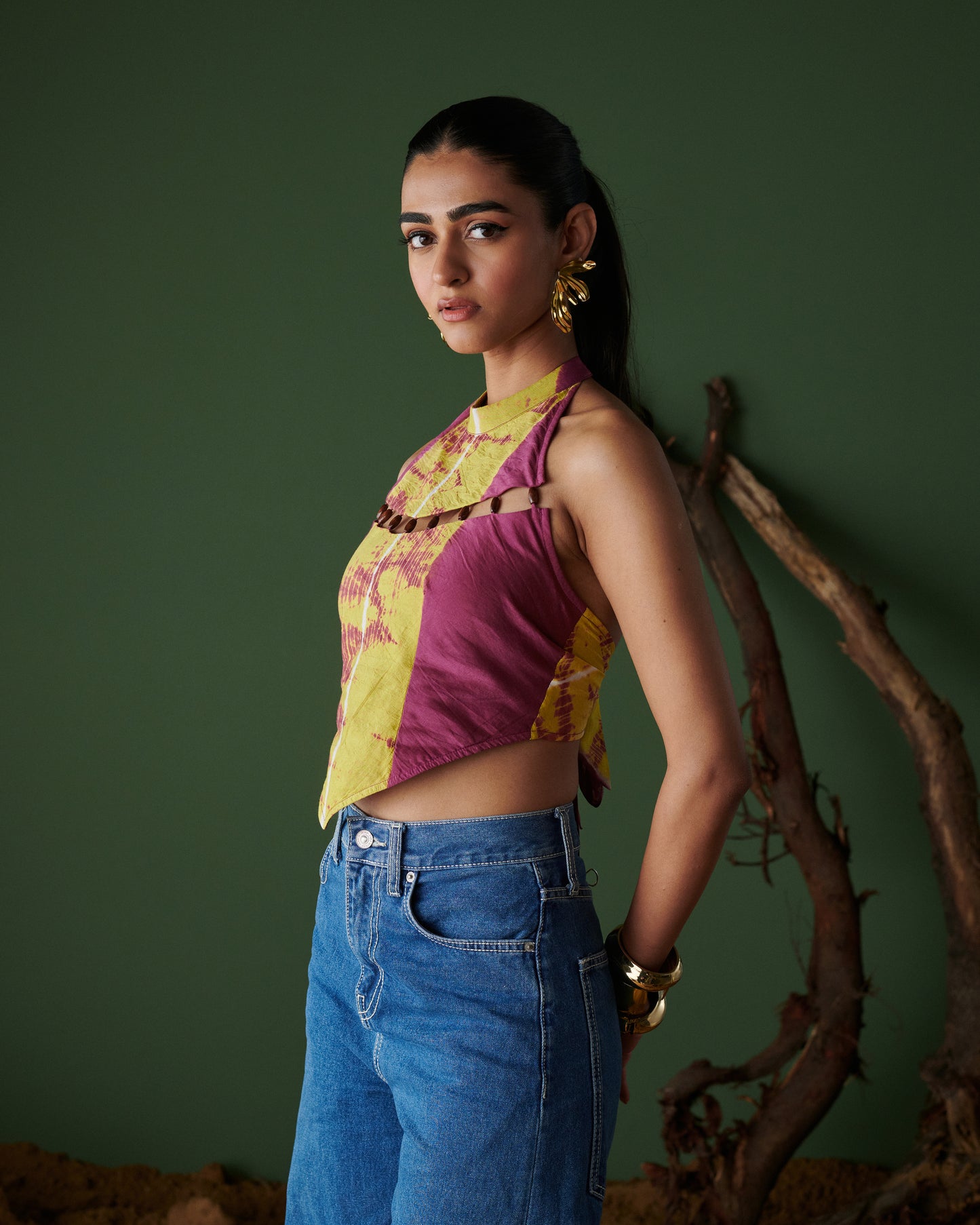 Side-profile view of Meetha Jaljeera Top in wine and deep yellow by Naarangi, a vibrant women’s halter-neck top with cut-out accents, hand-dyed using traditional techniques, styled with blue denim jeans, blending ethnic craftsmanship with modern boho-chic fashion in India.