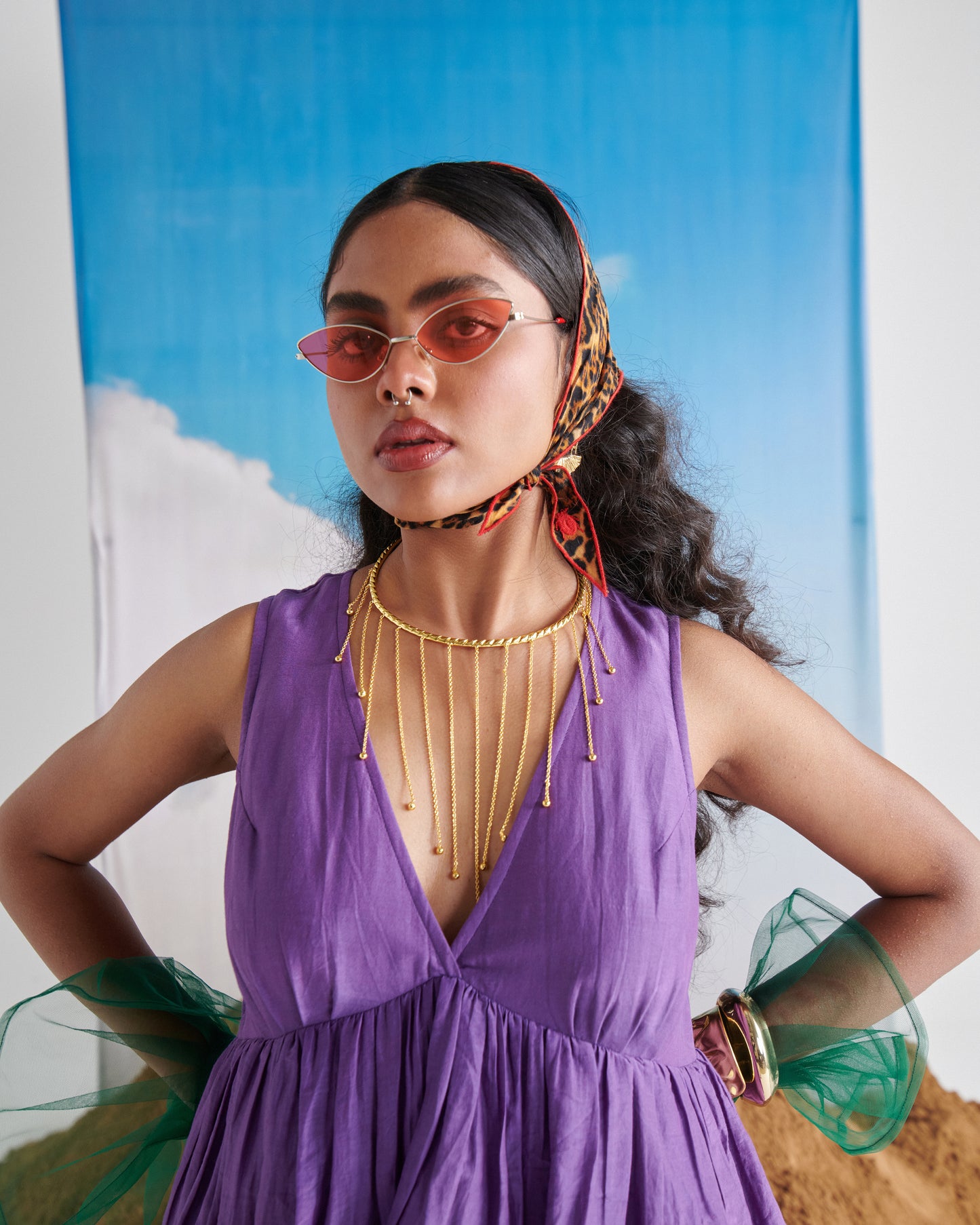 Model in Naarangi KalaKhatta purple maxi dress with jewelry and scarf, posing against blue sky backdrop.
