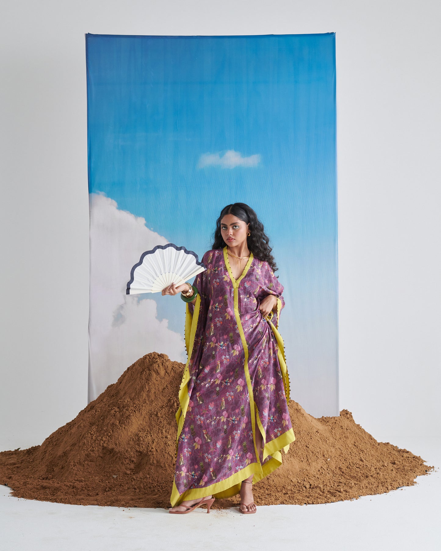 Front view of Plum Passion kaftaan holding a fan to the side, tropical print visible.
