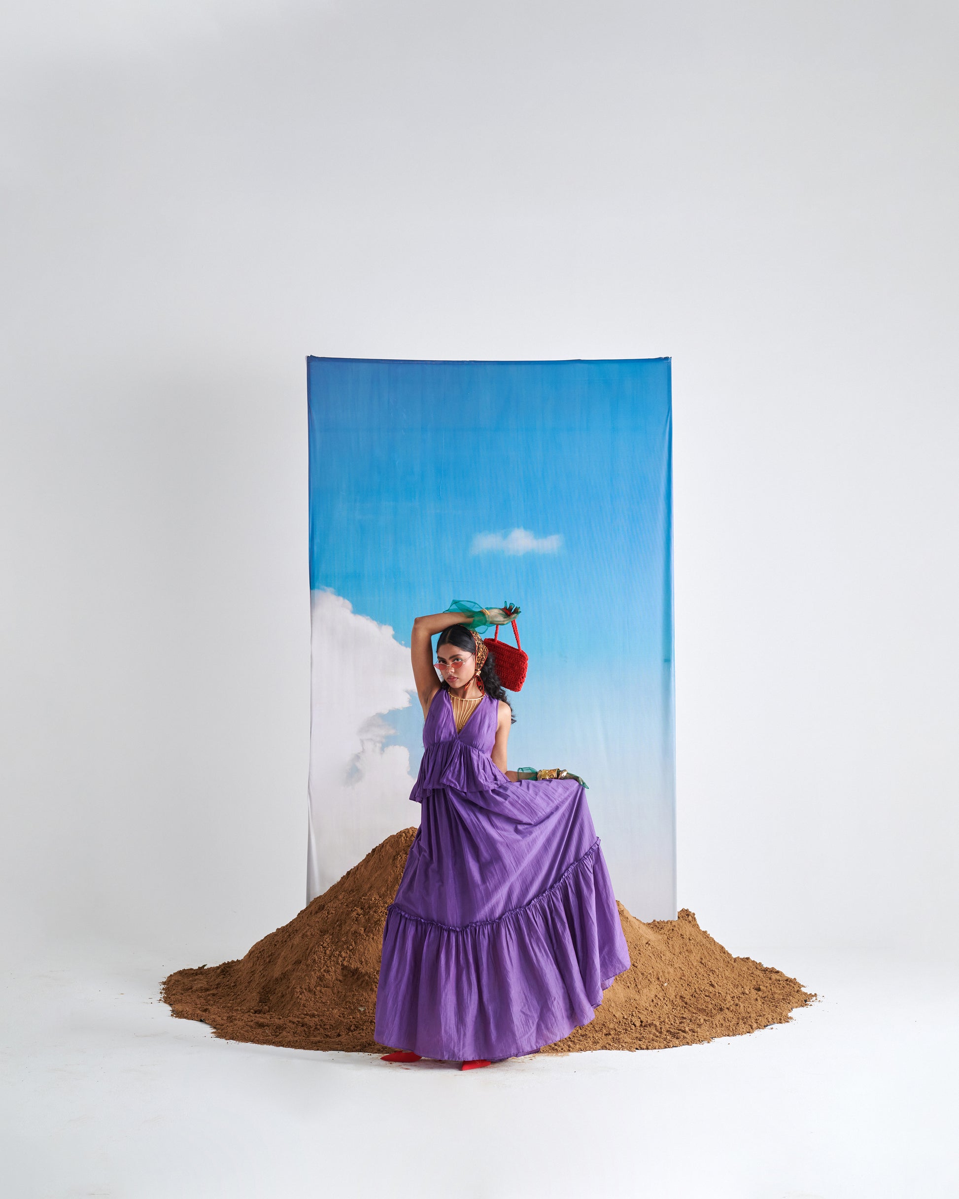 Model in KalaKhatta Crush Dress, purple maxi with layered tiers, styled with accessories and backdrop for editorial fashion shoot.