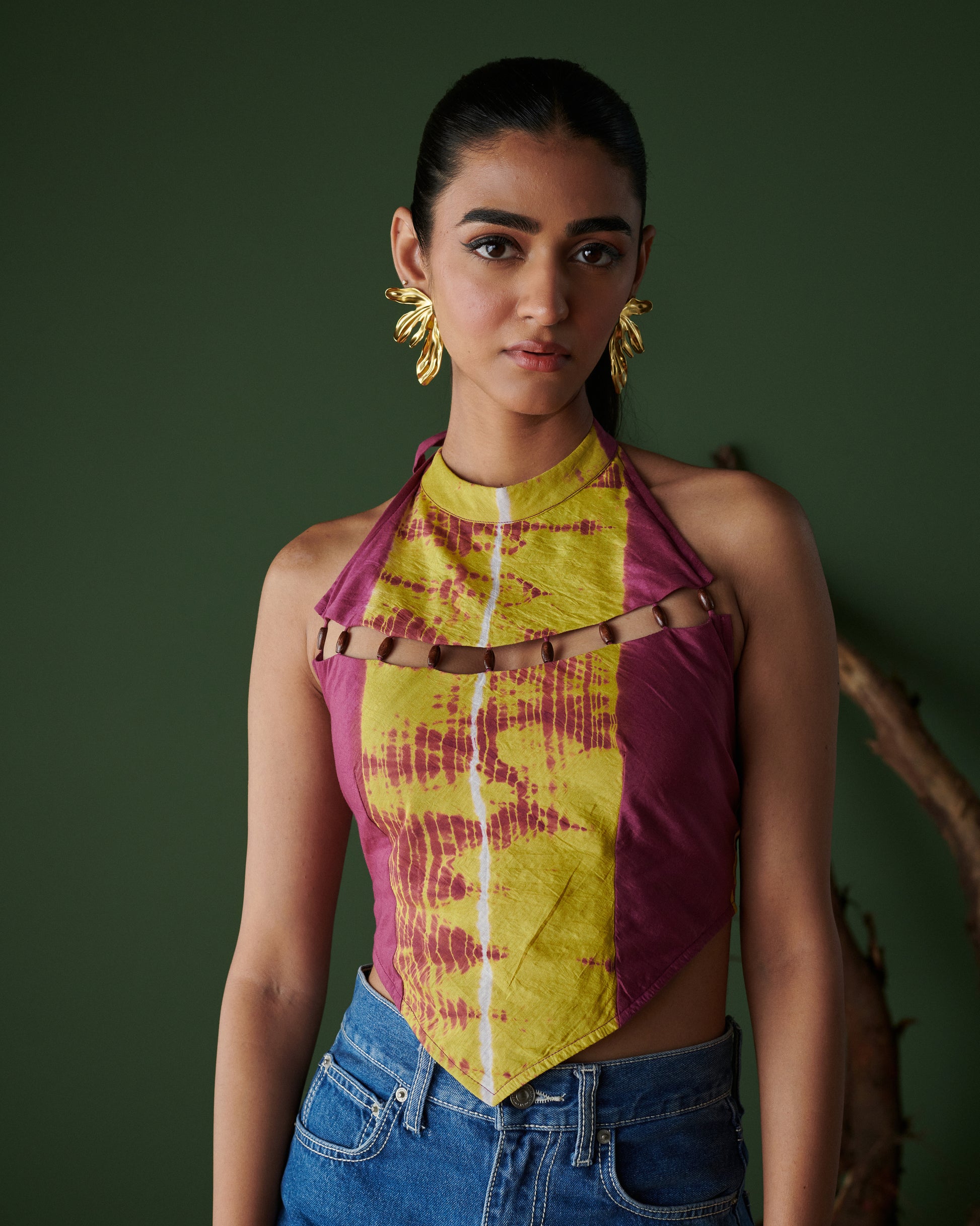 Close-up front view of Meetha Jaljeera Top in wine and deep yellow by Naarangi, a vibrant women’s halter-neck top with cut-out accents, hand-dyed using traditional techniques, styled with blue denim jeans, blending ethnic craftsmanship with modern boho-chic fashion in India.