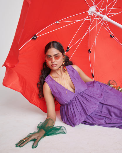Model wearing Naarangi KalaKhatta Crush Dress in purple, posing with red umbrella backdrop, styled with jewelry and green gloves.