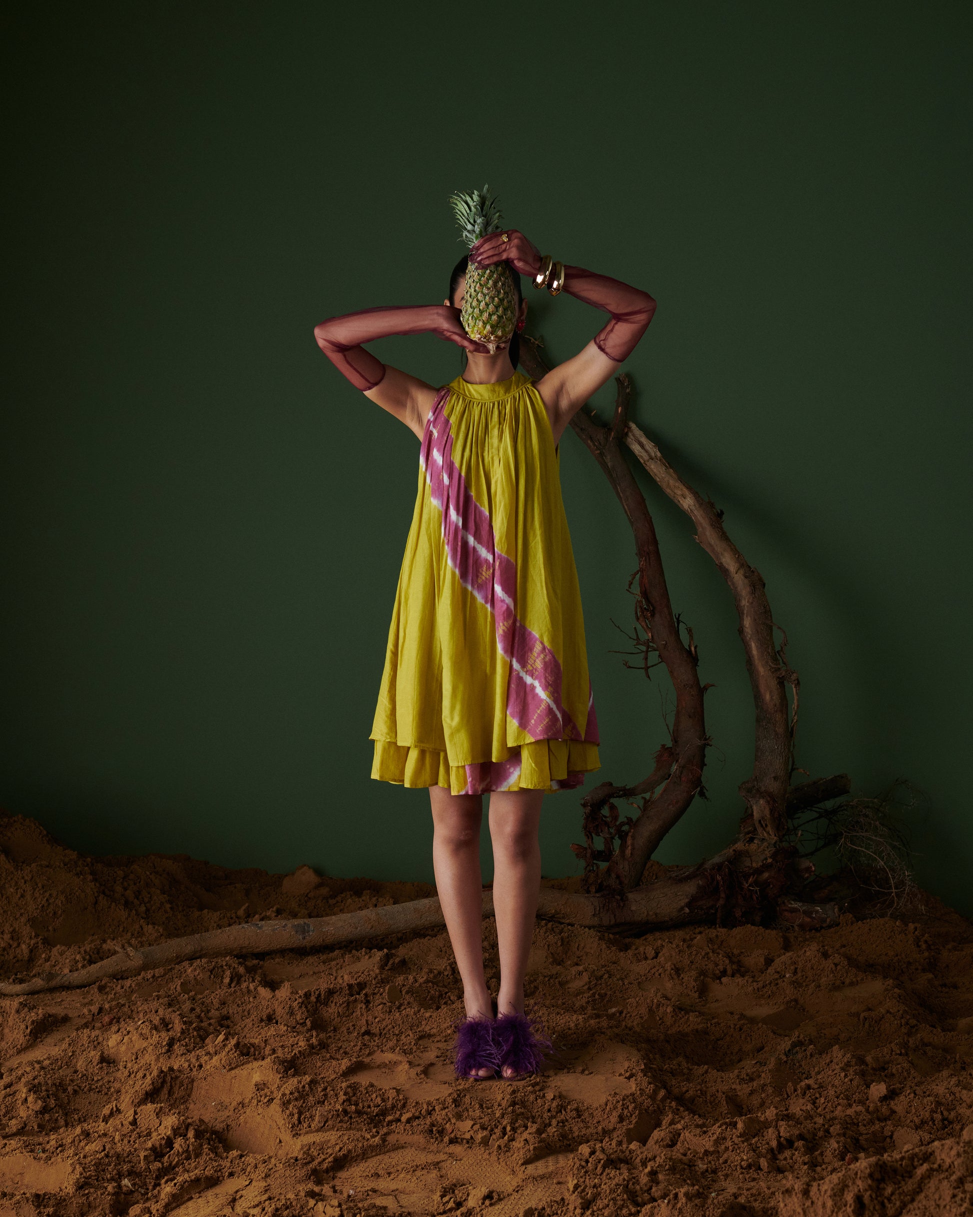 Model styling Naarangi Nimbu Twist yellow dress with purple heels and pineapple prop.