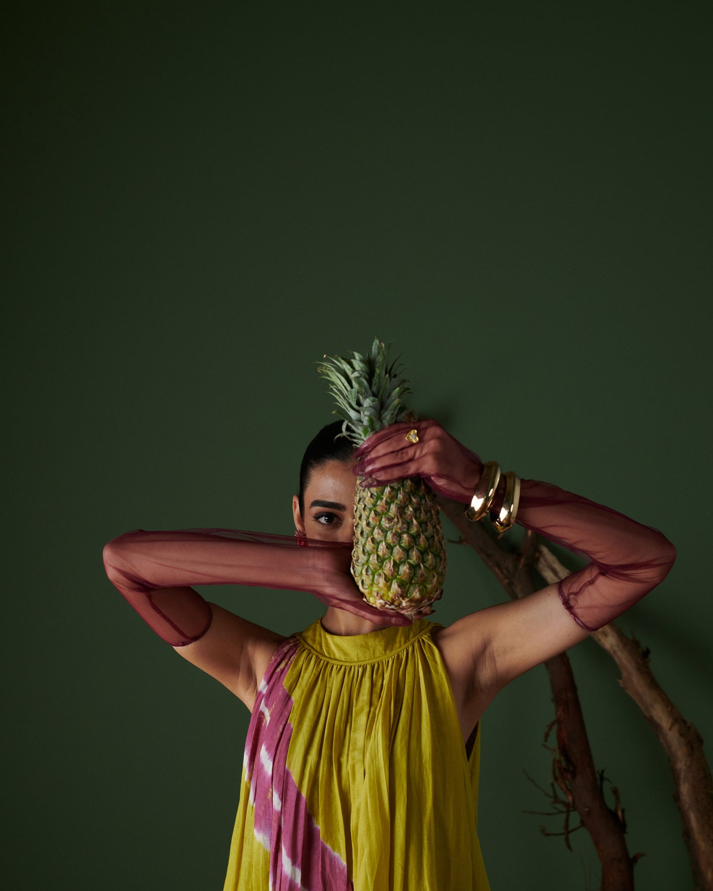 Fashion model posing in Naarangi Nimbu Twist yellow dress holding pineapple in front.
