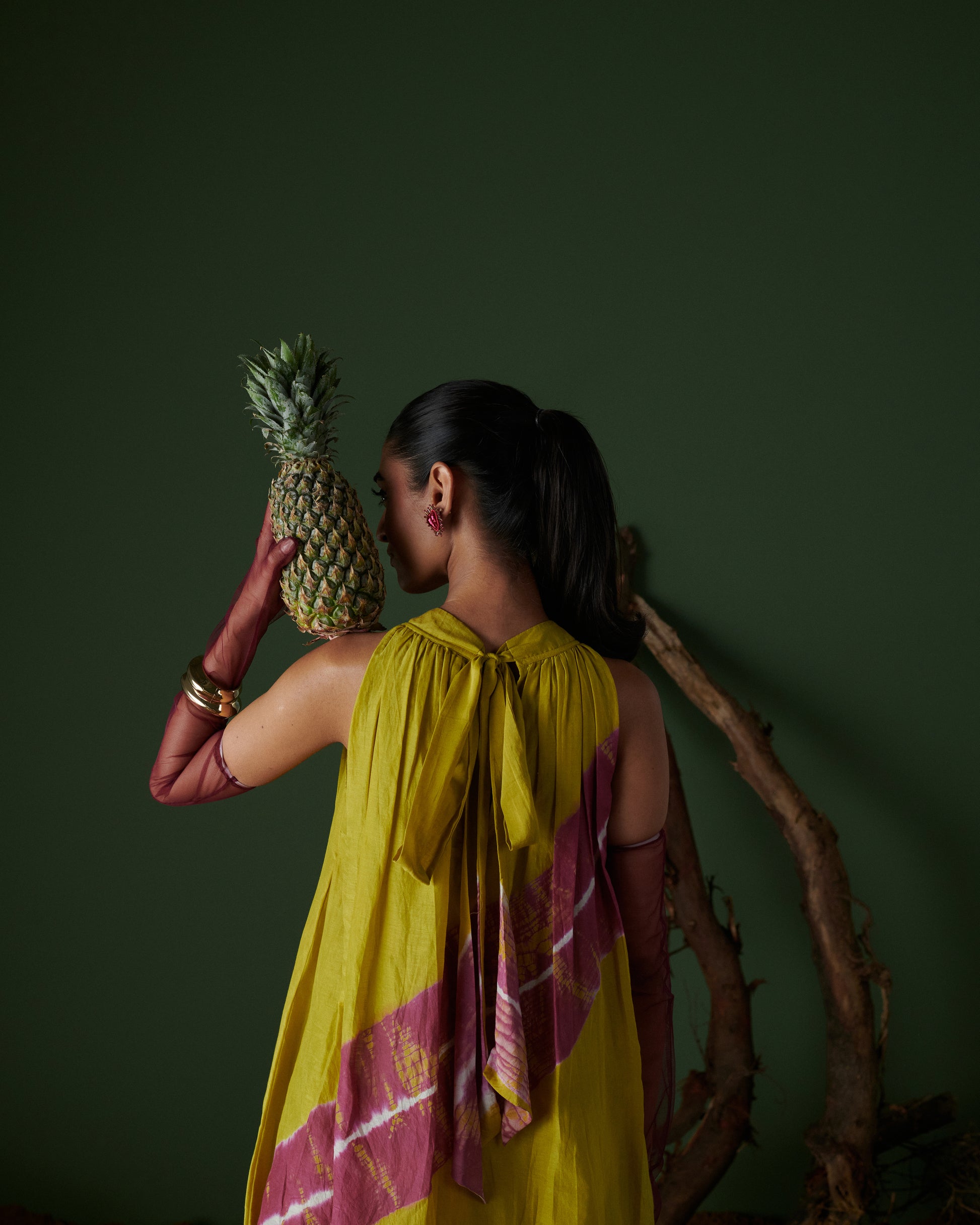 Woman in Naarangi Nimbu Twist yellow dress holding pineapple, stylish side profile.