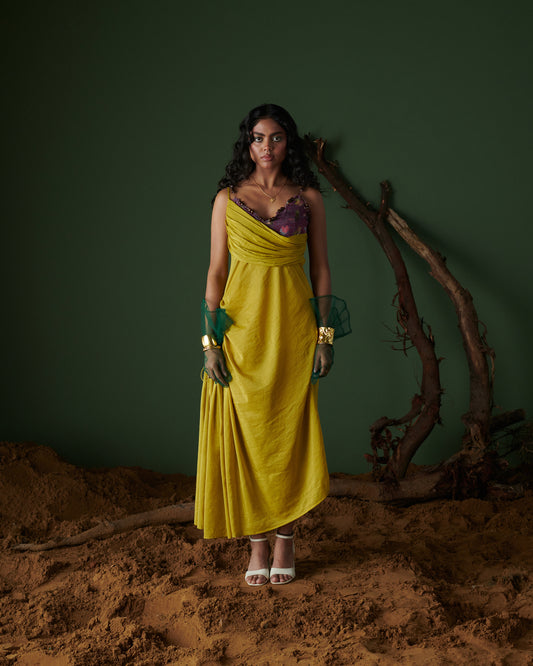 Model wearing Sunheri Zest draped yellow evening dress with purple inner and green gloves on earthy background.
