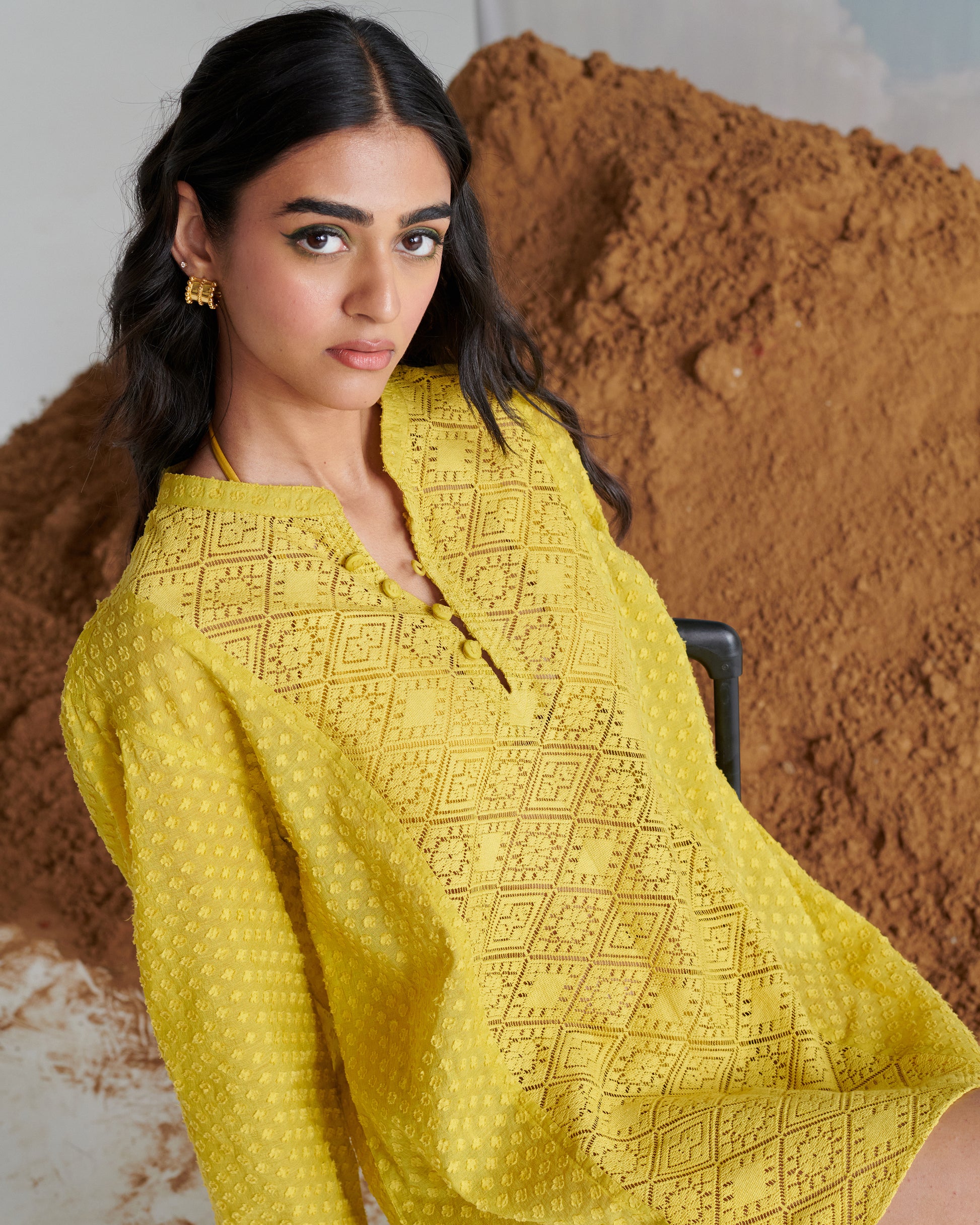 Close-up of Tangy Tadka Kurta in vibrant yellow, featuring intricate textured weave and button neckline in a reclining pose.
