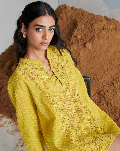 Close-up of Tangy Tadka Kurta in vibrant yellow, featuring intricate textured weave and button neckline in a reclining pose.